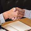 Two people shaking hands over a desk.