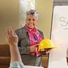 Older woman holding a hard hat standing infront of an easel that has Safety written on it.